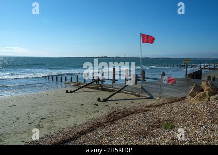 Sonne, Meer und Himmel, in East Head, West Wittering, Chichester Harbour, VEREINIGTES KÖNIGREICH. Defensive Groynes verlängern die Meeresrauschen. Die rote Flagge fliegt, um vor Gefahr zu warnen. Stockfoto