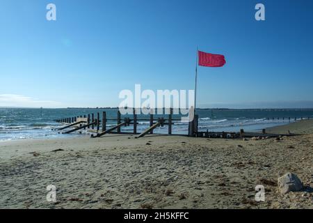 Sonne, Meer und Himmel, in East Head, West Wittering, Chichester Harbour, VEREINIGTES KÖNIGREICH. Defensive Groynes verlängern die Meeresrauschen. Die rote Flagge fliegt, um vor Gefahr zu warnen. Stockfoto