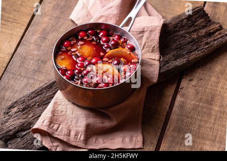 Heißer Glühwein aus Rotwein, Beeren und Orangen in einem Kupferkessel, Dekoration für Neujahr und Weihnachten Stockfoto