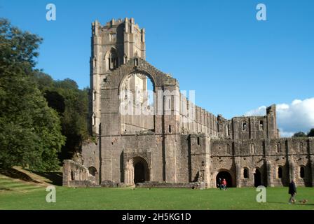 Menschen, die auf dem Gras vor dem Kirchenschiff und dem Großen Kreuzgang der Fountains Abbey, Aldfield, in der Nähe von Ripon, North Yorkshire, England, spazieren Stockfoto