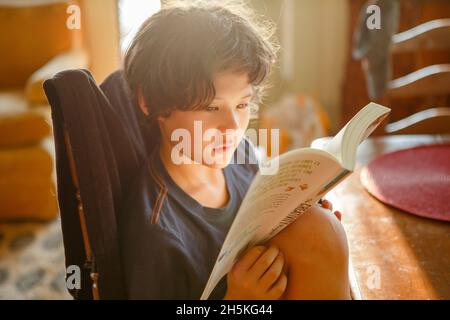 Ein schönes Kind liest im goldenen Morgenlicht ein Buch am Tisch Stockfoto