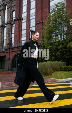 Junge Frau, die auf einer Fußgängerüberführung auf der Straße läuft Stockfoto