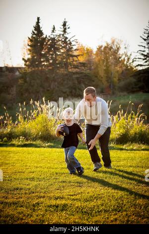 Vater spielt im Herbst mit seinem kleinen Sohn in einem Park Fußball; St. Albert, Alberta, Kanada Stockfoto