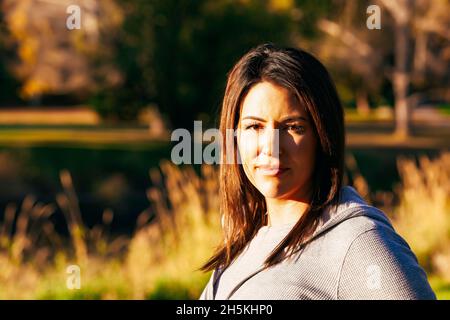 Außenportrait einer mittleren erwachsenen Frau mit brünetten Haaren, beleuchtet durch das Sonnenlicht im Herbst; St. Albert, Alberta, Kanada Stockfoto