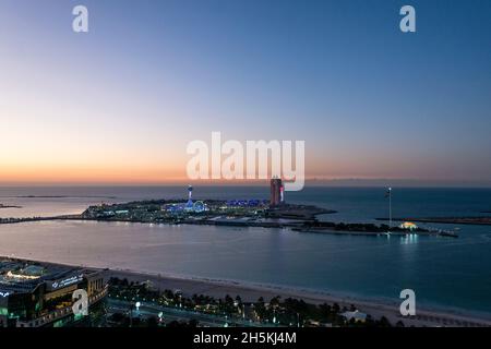 Die Sonne untergeht hinter Marina Island am Persischen Golf in Abu Dhabi, VAE. Ein Vergnügungspark scheint gegen die Dämmerung, als das ungeöffnete Atlantis Hotel si... Stockfoto