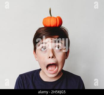 Porträt eines aufgeregten Jungen, der einen kleinen Kürbis auf seinen Kopf balanciert. Stockfoto
