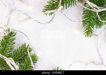 Grüne Tannenzweige und Lichter auf hellem Hintergrund mit Kopierfläche als Weihnachtsrahmen. Traditionelle Weihnachten und Winterferien Vorlage für Begrütin Stockfoto