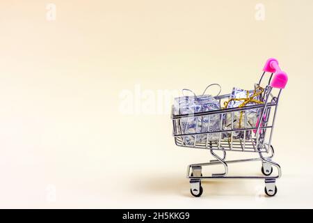 Trolley-Einkaufswagen mit silbernen Weihnachts- und Geburtstagschachteln für Geschenke und Geschenke auf hellem Hintergrund mit Kopierfläche. Weihnachtsangebot, Black Friday und Stockfoto