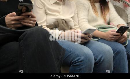 Nahaufnahme einer Frau, die in der U-Bahn in einem Telefon sitzt. Medien. Menschen, die in der U-Bahn fahren, verwenden Smartphones. Smartphone sucht in der Metro. Stockfoto