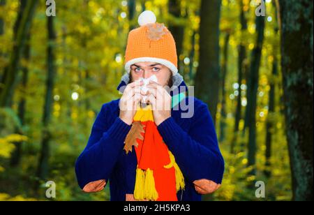 Kranker Mann im Herbstpark niest in Serviette. Guy hustet. Grippe, Krankheit, krank, Erkältung. Coronavirus-Epidemie. Männchen mit laufender Nase. Stockfoto