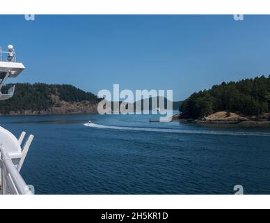 Ein kleines Wasserfahrzeug macht eine harte Steuerbordwende, um den Active Pass vor der Fähre zu betreten. Der Spirit of Vancouver Island liegt in der Ferne. Stockfoto