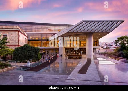 Das Akropolis-Museum im Zentrum von Athen, Griechenland, gegenüber dem Akropolis-Hügel. Panoramablick auf die Fassade bei Sonnenuntergang mit bunt bewölktem Himmel Stockfoto
