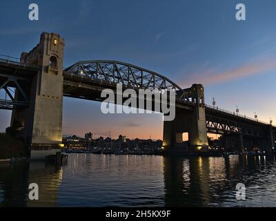 Burrard Street Bridge im Abendlicht nach Sonnenuntergang mit beleuchteten Säulen, die sich im Wasser der False Creek Bay in Vancouver, BC, Kanada, spiegeln. Stockfoto