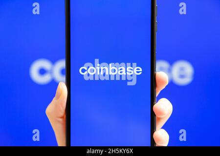 Ukraine, Odessa - Oktober, 9 2021: Hand hält Handy mit Coinbase App läuft auf dem Smartphone-Bildschirm mit Coinbase Logo im Hintergrund. Coinbase - Ame Stockfoto