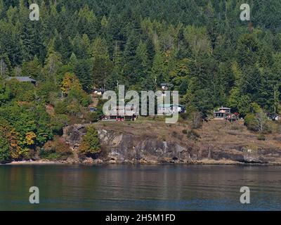 Ruhige Landschaft mit Wohngebäuden an der rauen Küste von Galiano Island, Salish Sea, British Columbia, Kanada im Herbst umgeben von Wald. Stockfoto