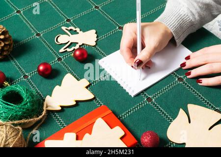 Eine Frau schreibt eine Weihnachtsliste mit Geschenken oder To-Do's in einem Notizbuch in festlicher Atmosphäre. Vorbereitung auf die Feier. Stockfoto