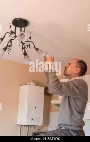 Mann, der eine energiesparende Glühbirne in einem Kronleuchter wechselt Stockfoto