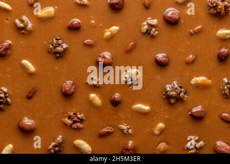 Geschmolzene Karamellsauce mit verschiedenen Nüssen, Bild im Vollformat. Draufsicht auf spröde Erdnussbestandteile. Karamellisierte Haselnüsse und Erdnüsse in Karamellsirup Stockfoto