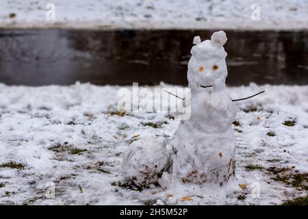 Ein Schneemann, geblendet von Kindern vom ersten Schnee, der auf den Hintergrund einer Joggingstraße im Park fiel. Stockfoto