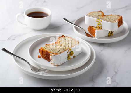 Zitronenkuchen mit Mohnsamen, bedeckt mit Glasur auf hellem Hintergrund und Kaffee Stockfoto