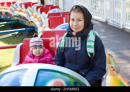 Teenager-Mädchen mit ihrer kleinen Schwester, die Zug auf dem Spielplatz im Vergnügungspark fährt, sitzt zusammen in der Kabine, Herbst Stockfoto