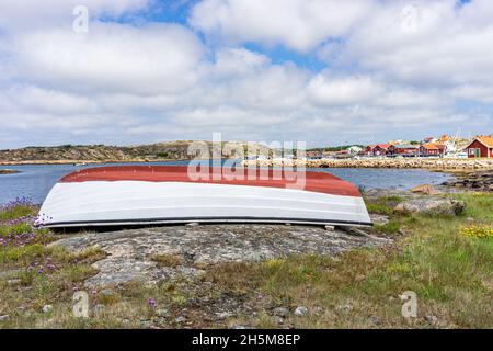 Smögen, Schweden - 9. Juni 2021: Verlassene weiße und rote Boote an der Bucht mit Dorfhintergrund Stockfoto