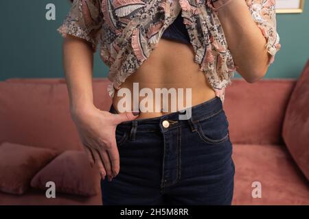 Gewichtsverlust und Body Image Konzept. Junge Frau zeigt ihren Gewichtsverlust und trägt ihre alte Jeans. Slim Girl in Big Jeans zeigt, wie sie Wei verlor Stockfoto