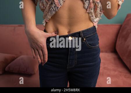 Gewichtsverlust und Body Image Konzept. Junge Frau zeigt ihren Gewichtsverlust und trägt ihre alte Jeans. Slim Girl in Big Jeans zeigt, wie sie Wei verlor Stockfoto