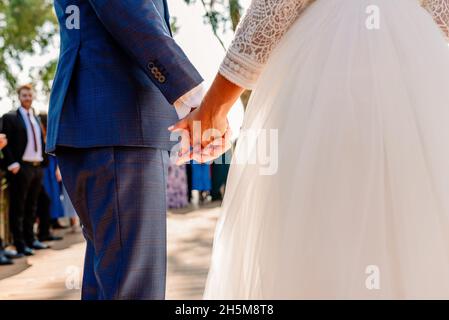 Ein frisch verheiratetes Paar beginnt an ihrem Hochzeitstag mit der Zeremonie und hält sich die Hände. Stockfoto
