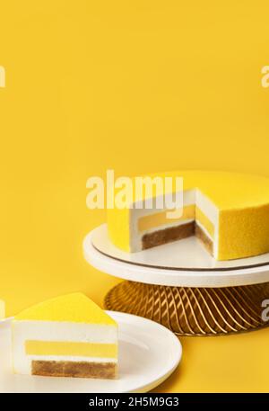 Köstlicher Mango- und Passionsfrucht-Mousse-Kuchen auf einem Ständer und mit den Schichten und der Textur auf hellgelbem Hintergrund in Scheiben schneiden. Restaurant-Menü und Süßwarenkonzept. Nahaufnahme. Speicherplatz kopieren. Stockfoto