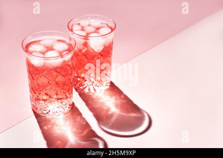 Zwei wunderschöne Kristallgläser werfen lange Schatten vom Sonnenlicht auf weißen und rosa Hintergrund. Minimale kreative Komposition mit Kopierplatz. Sommergetränke-Konzept. Stockfoto