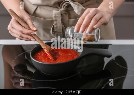 Frau kocht Bio-Tomatensauce in der Pfanne auf Herd in der Küche Stockfoto