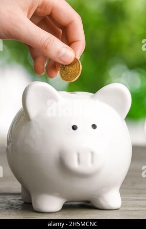 Frau, die im Freien eine goldene Münze in ein Sparschwein auf den Tisch legt Stockfoto