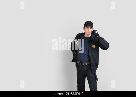 Junger Polizist mit Taschenlampe auf hellem Hintergrund Stockfoto