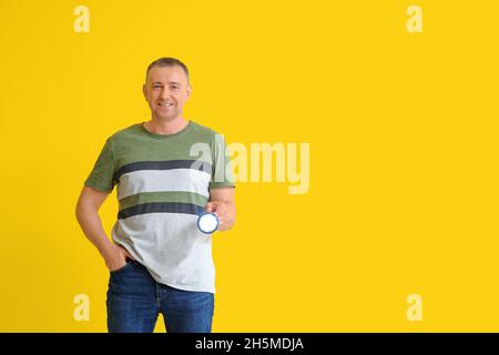 Reifer Mann mit Taschenlampe auf gelbem Hintergrund Stockfoto