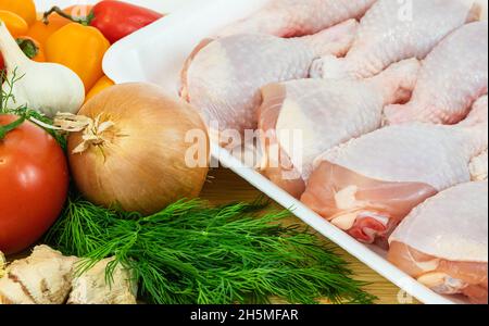 Rohe Hähnchendrumsticks mit Gemüse bereit zum Kochen. Frisches rohes Hühnerbein an Bord mit Gemüse Stockfoto