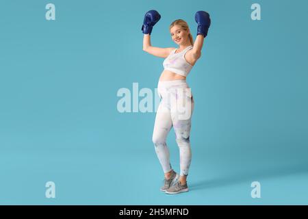 Sportliche junge Schwangere in Boxhandschuhen auf blauem Hintergrund Stockfoto