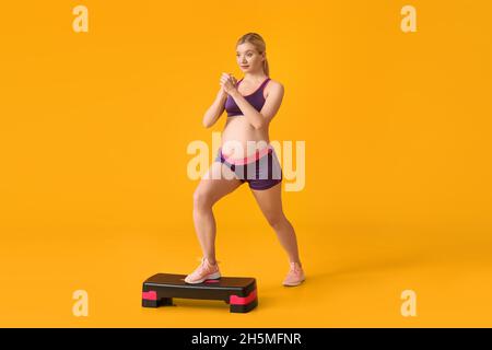 Junge Schwangeren trainieren mit Aerobic Stepper auf gelbem Hintergrund Stockfoto