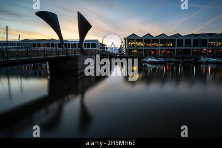 Die Sonne untergeht über der Pero's Bridge und den Lagerhallen an der erneuerten Harbourside in Bristol. Stockfoto