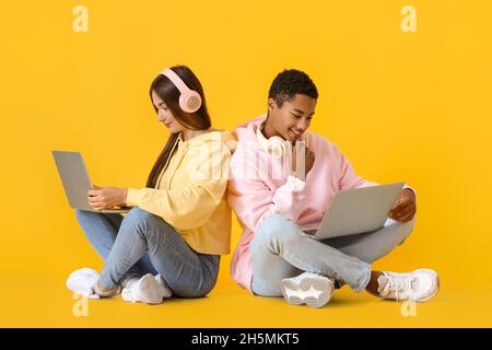 Stilvolles junges Paar in Hoodies mit Laptops auf gelbem Hintergrund Stockfoto