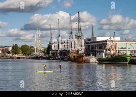 Paddelboarder paddeln über den schwimmenden Hafen von Bristol, mit historischen Schiffen, die vor dem M Shed Museum hinter dem Hotel angedockt sind. Stockfoto