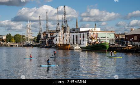 Paddelboarder paddeln über den schwimmenden Hafen von Bristol, mit historischen Schiffen, die vor dem M Shed Museum hinter dem Hotel angedockt sind. Stockfoto