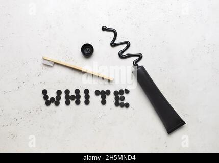 Geöffnete Tube mit Aktivkohle-Zahnpasta, Zahnbürste und Word WHITE aus Pillen auf hellem Hintergrund Stockfoto