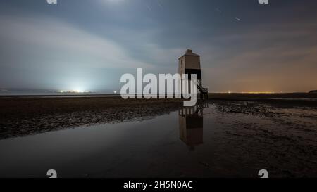 Der Leuchtturm in niedriger Höhe steht am Sandstrand von Burnham-on-Sea, am Ufer des Bristol Channel in Somerset, mit den Lichtern von South Wales Stockfoto