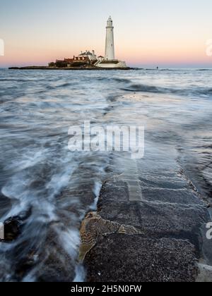 Wellen, Strömung gegenüber der St. Maria Island Causeway in der Dämmerung, mit St Mary's Leuchtturm hinter, auf der Whitley Bay Küste von Tyneside. Stockfoto