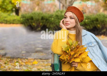 Schöne verträumte Frau mit Herbststrauß sitzt auf Bank im Park Stockfoto