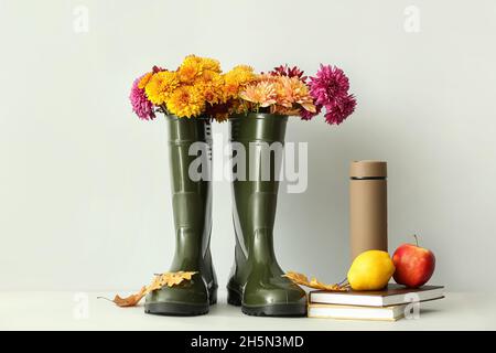 Gummistiefel mit Blumen, Thermoskannen, Büchern und Früchten auf weißem Hintergrund Stockfoto