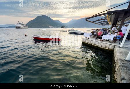 Perast,Montenegro-7. September 2019: Bei Sonnenuntergang essen die Gäste Meeresfrüchte, während ein Schiff auf die Abfahrt wartet, um Touristen in die Adria zu bringen. Stockfoto