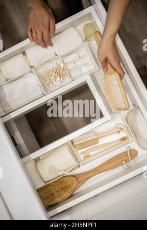 Die Frau hält eine Holzbürste in der Hand und legt sie zusammen mit den Toilettenartikeln in die Schublade. Stockfoto