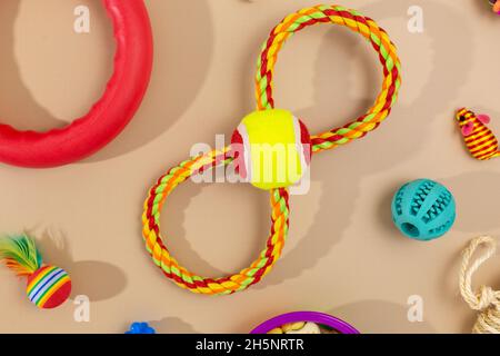 Verschiedene bunte Tierpflegezubehör: Schale, Knochen, Kugeln, Snacks, Maus auf beigem Hintergrund. Gummi- und Textilzubehör für Hunde und Katzen. Stockfoto